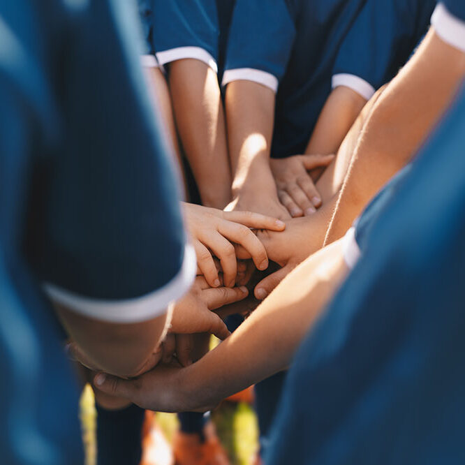 Sports team stacking hands together in a group. Happy children teammates motivated in a team. Team building activities and boosting sports players' morale